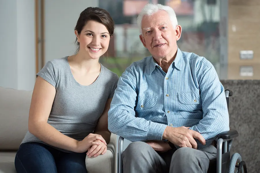Older man in a wheelchair with a woman sitting on a couch in front of him