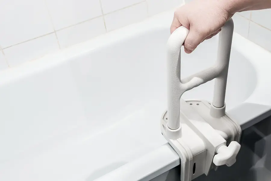 Person holding a white bathtub grab bar in their hand, with a wall in the background