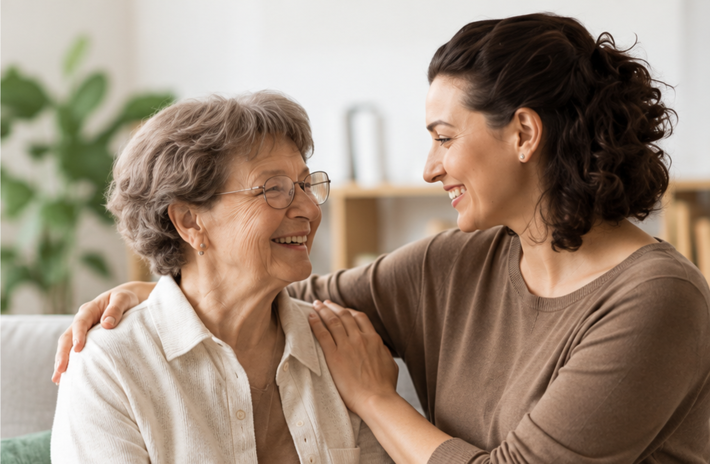 Older woman sitting on a couch with her caregiver, both of them The background is slightly blurred