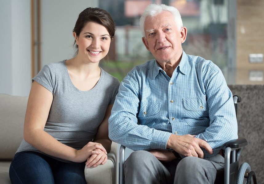Older man in a wheelchair with a woman sitting on a couch in front of him