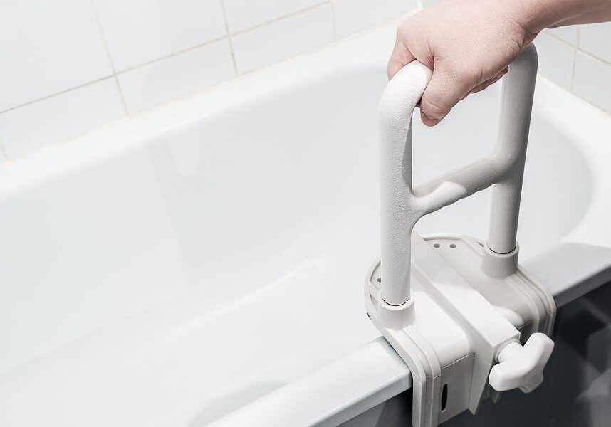 Person holding a white bathtub grab bar in their hand, with a wall in the background